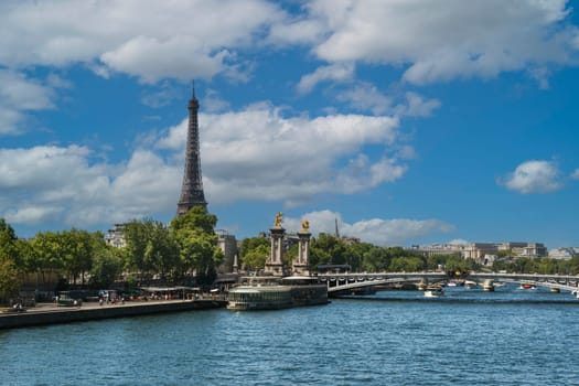 View of the Seine River in Paris with the Eiffel Tower in the background on a summer day with blue sky and white clouds.