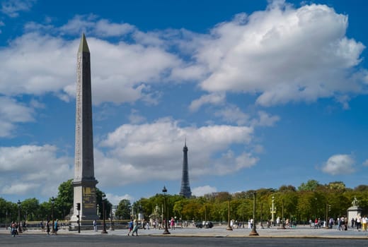 View of the Place de la Concorde in Paris with the obelisk of Luxor and the Eiffel Tower in the background on a summer day with blue sky and white clouds.