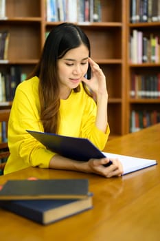 Pleased female student reading book in a library for studying and research. Education, learning, knowledge and university.