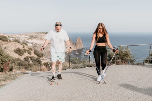 Happy Middle aged couple or friends practicing nordic walking in park near sea. Mature couple with trekking poles walking, practicing Nordic walking outdoors. Aging youthfully and sport concept.