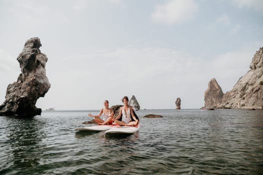 Woman sup yoga. Middle age sporty woman practising yoga pilates on paddle sup surfboard. Female stretching doing workout on sea water. Modern individual hipster outdoor summer sport activity