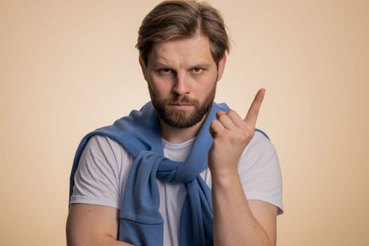 Quarrel. Displeased young caucasian man gesturing hands with irritation and displeasure, blaming scolding for failure, asking why this happened. Bearded adult guy isolated on beige studio background