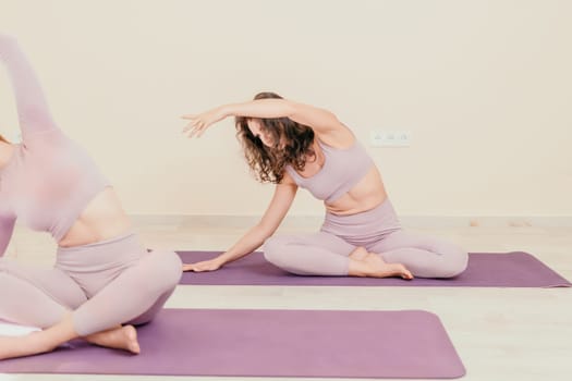 Young woman with long hair in white swimsuit and boho style braclets practicing outdoors on yoga mat by the sea on a sunset. Women's yoga fitness routine. Healthy lifestyle, harmony and meditation