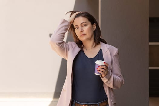 Puzzled Sad Mature 40 yo Woman Holds Cup OF Coffee, Looking At Camera Outside, Tired, Worried Nervous Caucasian Brunette Female Wears Casual Cloth. Horizontal Plane, Copy Space. High quality photo