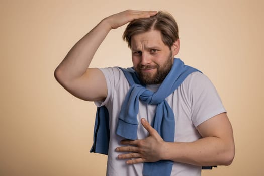 Comical funny young caucasian man making playful silly facial expressions and grimacing, fooling around. Handsome crazy adult guy bullying isolated on studio beige background indoors