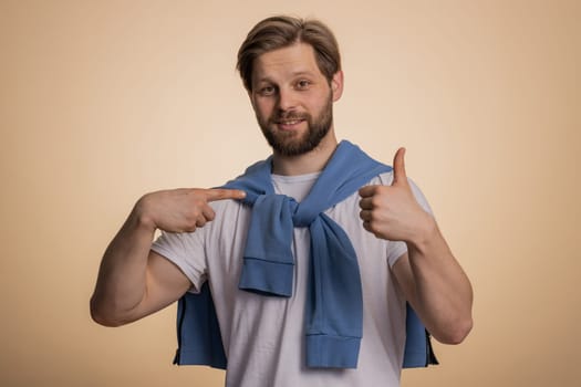 I am the best, choose me. Young excited caucasian man winner feeling very proud pointing hisself, looking self-confident, overjoyed by success. Handsome adult guy isolated on studio beige background