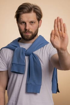 Angry man say No hold palm folded crossed hands in stop gesture, warning of finish, prohibited access, declining communication, body language, danger. Young guy on beige background. People lifestyle