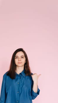 Young Businesswoman in Blue Shirt Pointing at Mockup, Symbolizing Office Promotion and New Opportunities: Professional Portrait on Pink Background.