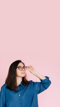 Thoughtful Woman in Glasses, Touching Her Frames, Deep in Contemplation, Searching for Ideas in Empty Space: Isolated Pink Background Portrait.