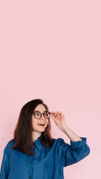 Smiling woman touching glasses, pondering and looking for ideas in empty space: Isolated portrait on pink background.