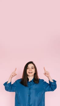 Vibrant Portrait of Energetic Young Woman Expressing Amazement with Open Mouth and Pointing Fingers Upward, Isolated on Pink Background.