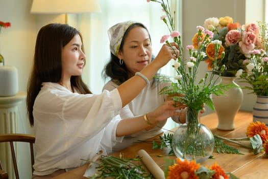 Pretty young asian woman and her senior mother arranging flowers, spending good time together at home.