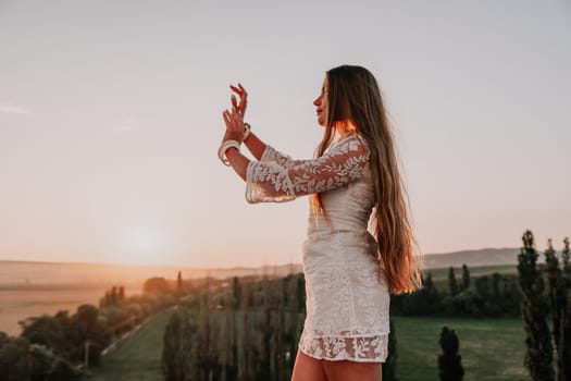 Romantic beautiful bride in white dress posing with sea and mountains in background. Stylish bride standing back on beautiful landscape of sea and mountains on sunset