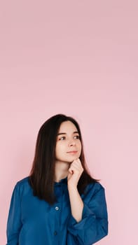 Serenity and Contemplation: Mindful Portrait of a Beautiful Girl with Hand on Chin, Gazing into Empty Space, Isolated on a Calming Pink Background. Vertical photography.