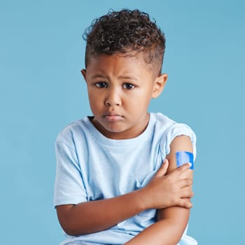 Portrait, sad and kid with arm bandage in studio isolated on a blue background. Face, upset and child with plaster after vaccine, injury or wound for healthcare wellness, first aid or medical help
