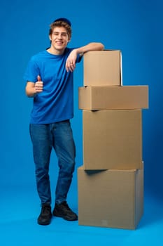 Young male courier in a blue uniform holds parcel in his hands in studio