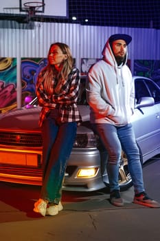 Smiling loving couple standing near sport car over night city background