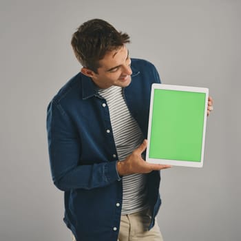 Click onto our website and see for yourself. Studio shot of a young man holding a digital tablet with a green screen against a grey background