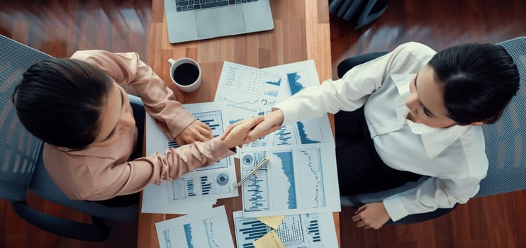 Top view asian businesswomen shaking hands over desk in modern office after successfully analyzing pile of dashboard data papers as modern teamwork and integrity in the workplace concept. Enthusiastic