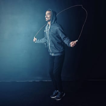 Its an all-body workout. Studio shot of a young man skipping against a dark background