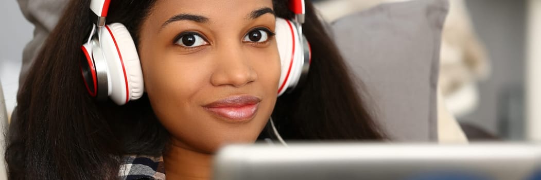 Smiling african american woman in headphones with laptop sitting on sofa at home. Listening to music or watching movies concept