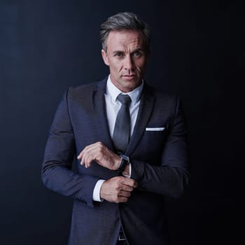 Purpose driven style. Studio portrait of a stylish and mature businessman standing against a dark background