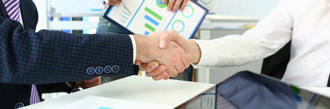 Handshake of business people at meeting and signing agreement. Working group of team at conference discusses financial chart and concludes business contract