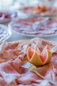 Plate of cooked ham with orange as decoration. Party, holiday. Defocused background.