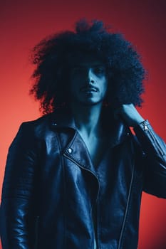 Portrait of fashion man with curly hair on red background multinational, colored light, black leather jacket trend, modern concept. High quality photo