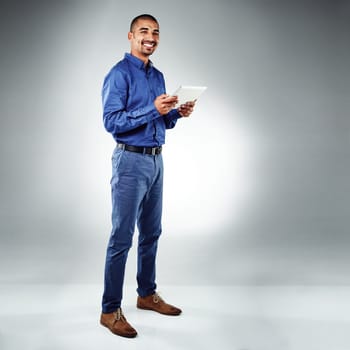 Hes curious and adventurous in his business pursuit. Studio shot of a young businessman using his tablet against a grey background