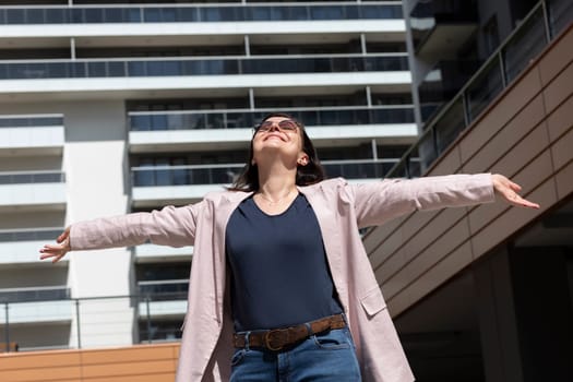 Happy Mature Woman With Open Arms Enjoys Modern Residential Building, Standing In New Apartment Campus, Complex In Sunny Day. Female Brunette Wears Casual Cloth, Horizontal, Real Estate Development.