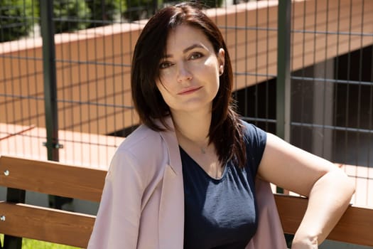 Portrait Beautiful Brunette Mature Woman Sitting On A Bench In Residential Campus. Female Is Dressed In Casual Clothes. Rest And Relaxation. Horizontal Plane. High quality photo