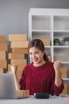 Startup small business entrepreneur SME or freelance Asian woman using a laptop with box, Young success Asian woman with her hand lift up, online marketing packaging box and delivery, SME concept...