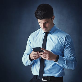 The best connections are instant connections. Studio shot of a young businessman texting on a cellphone against a dark background
