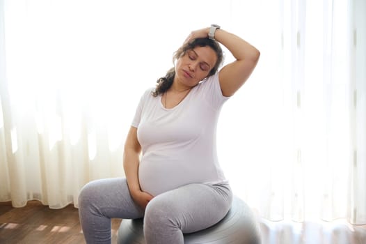 Gravid expectant woman, future mom expecting baby, practicing prenatal stretching exercising on fit ball. Sport. Fitness. Active healthy lifestyle in pregnancy time for easy childbirth and pain relief