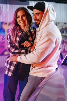 Smiling loving couple standing near sport car over night city background