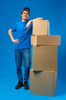 Young male courier in a blue uniform holds parcel in his hands in studio