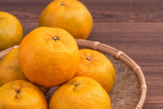 Fresh, beautiful orange color tangerine on bamboo sieve over dark wooden table. Seasonal, traditional fruit of Chinese lunar new year, close up.