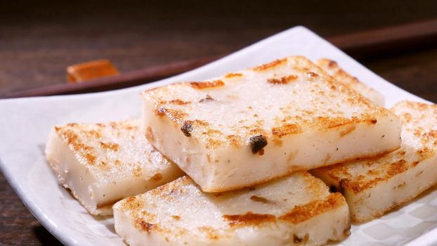 Pouring black soy sauce on ready-to-eat delicious turnip cake, Chinese traditional local dish radish cake in restaurant, close up, copy space.