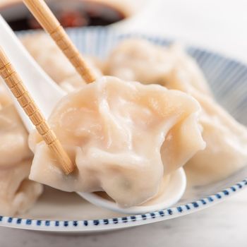 Fresh, delicious boiled pork, shrimp gyoza dumplings on white background with soy sauce and chopsticks, close up, lifestyle. Homemade design concept.