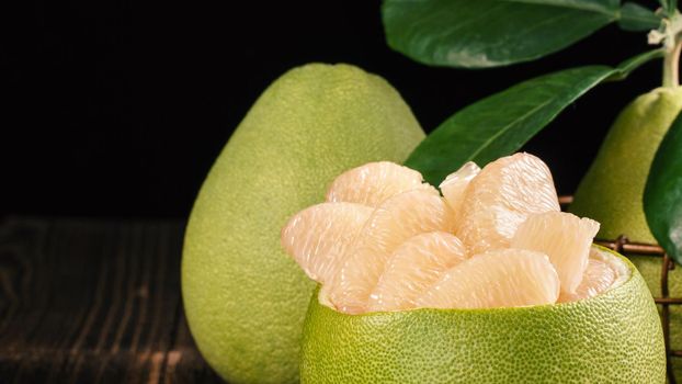Fresh peeled pomelo, grapefruit, shaddock with green leaves on dark wooden plank table. Seasonal fruit near mid-autumn festival, close up, copy space