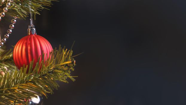 Beautiful Christmas decor concept, bauble hanging on the Christmas tree with sparkling light spot, blurry dark black background, macro detail, close up.