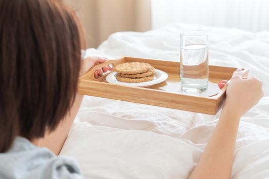 Woman holding tray with diet breakfast of crackers and water on bed