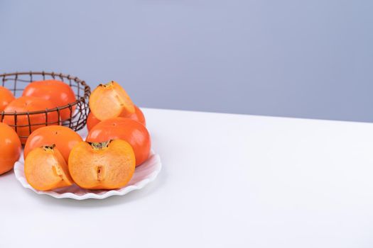 Fresh beautiful sliced sweet persimmon kaki isolated on white kitchen table with gray blue background, Chinese lunar new year design concept, close up.