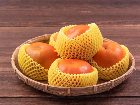 Fresh, beautiful orange color persimmon kaki on bamboo sieve over dark wooden table. Seasonal, traditional fruit of Chinese lunar new year, close up.