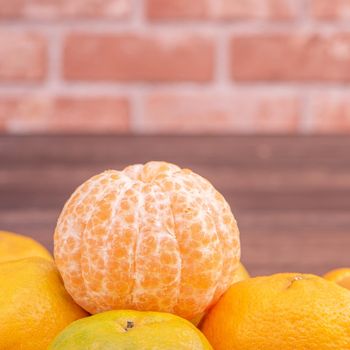 Peeled tangerines in a bamboo sieve basket on dark wooden table with red brick wall background, Chinese lunar new year fruit design concept, close up.