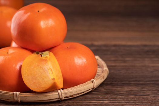 Fresh, beautiful orange color persimmon kaki on bamboo sieve over dark wooden table. Seasonal, traditional fruit of Chinese lunar new year, close up.