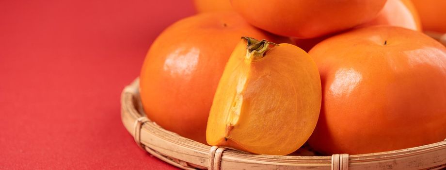 Fresh beautiful sliced sweet persimmon kaki isolated on red table background and bamboo sieve, Chinese lunar new year design concept, close up.