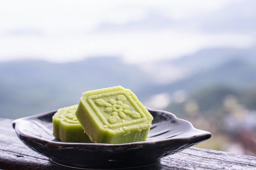 Delicious green mung bean cake with black tea plate on wooden railing of a teahouse in Taiwan with beautiful landscape in background, close up.