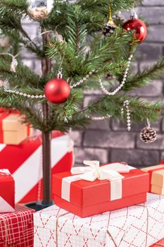 Decorated Christmas tree with wrapped beautiful red and white gifts at home with black brick wall, festive design concept, close up.